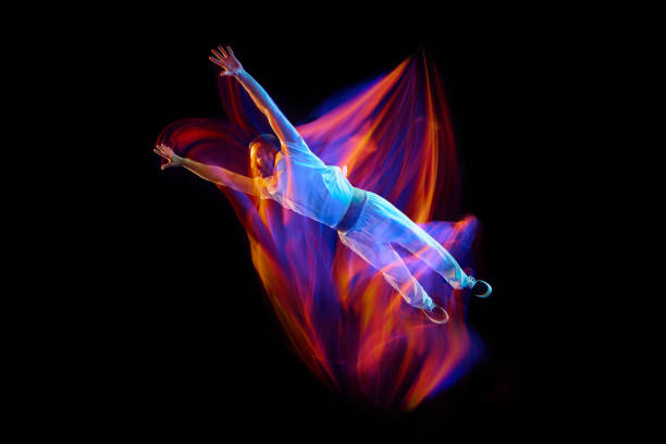 Dance in motion. Studio shot of flying, jumping dancer or gymnast performing tricks in the air over black background with mixed neon glowing rays Dance in motion. Studio shot of flying, jumping dancer or gymnast performing tricks in the air over black background with mixed neon glowing rays. Fantasy, cyberpunk, sport, fashion hyperdrive stock pictures, royalty-free photos & images