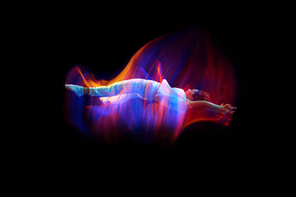 Dance in motion. Studio shot of flying, jumping dancer or gymnast performing tricks in the air over black background with mixed neon glowing rays Dance in motion. Studio shot of flying, jumping dancer or gymnast performing tricks in the air over black background with mixed neon glowing rays. Fantasy, cyberpunk, sport, fashion hyperdrive stock pictures, royalty-free photos & images