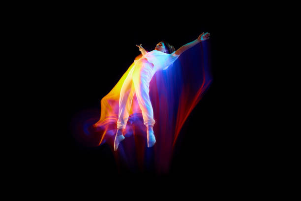 Levitation. One flying, jumping dancer or gymnast performing tricks in the air over black background with mixed neon glowing rays Levitation. One flying, jumping dancer or gymnast performing tricks in the air over black background with mixed neon glowing rays. Fantasy, cyberpunk, sport, fashion hyperdrive stock pictures, royalty-free photos & images