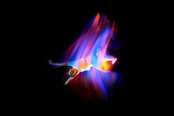 Dance in motion. Studio shot of flying, jumping dancer or gymnast performing tricks in the air over black background with mixed neon glowing rays Dance in motion. Studio shot of flying, jumping dancer or gymnast performing tricks in the air over black background with mixed neon glowing rays. Fantasy, cyberpunk, sport, fashion hyperdrive stock pictures, royalty-free photos & images