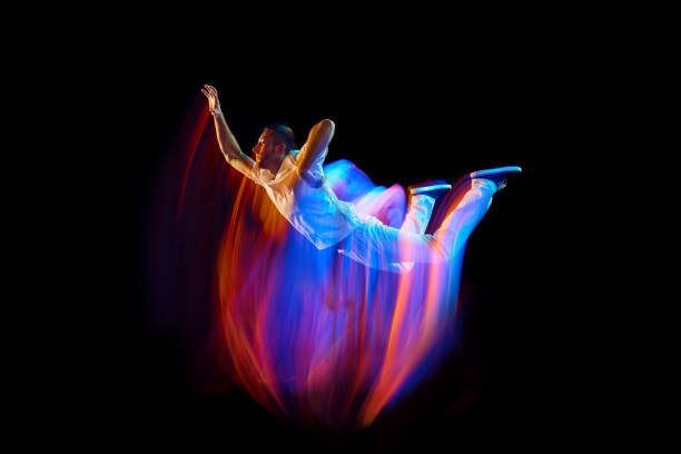 Levitation. One flying, jumping dancer or gymnast performing tricks in the air over black background with mixed neon glowing rays Levitation. One flying, jumping dancer or gymnast performing tricks in the air over black background with mixed neon glowing rays. Fantasy, cyberpunk, sport, fashion hyperdrive stock pictures, royalty-free photos & images