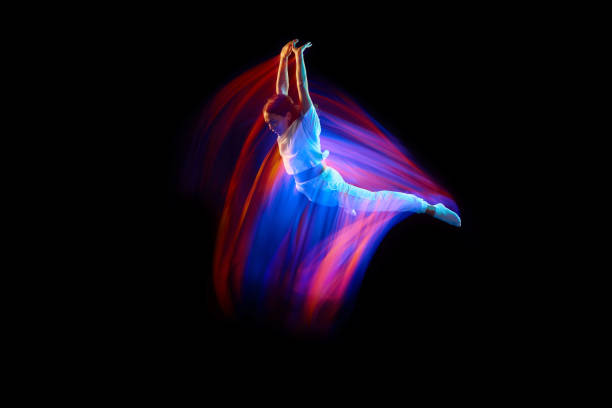 Levitation. One flying, jumping dancer or gymnast performing tricks in the air over black background with mixed neon glowing rays Levitation. One flying, jumping dancer or gymnast performing tricks in the air over black background with mixed neon glowing rays. Fantasy, cyberpunk, sport, fashion hyperdrive stock pictures, royalty-free photos & images