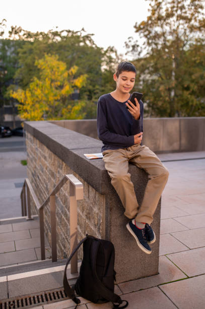 istock Joyous boy seated outdoors using his smartphone 1435071825