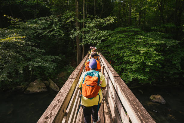 women crossing the bridge over a river as they head out hiking stock photo