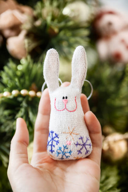 Woman holds cute handmade rabbit with embroidered snowflakes. DIY decoration for Christmas tree. Present or souvenir, symbol of New Year 2023 year. stock photo