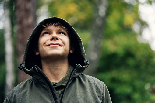 Portrait of a cute teenage boy hiker on a rainy autumn day. The boy is smiling and looking up.\nCanon R5