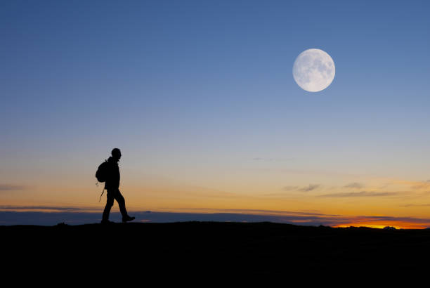 夕暮れ時に満月の下を歩くハイカー。 - walking night men sunset ストックフォトと画像