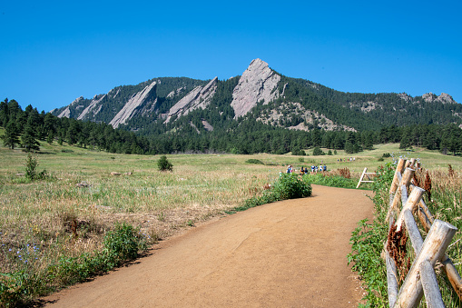 A hiking trail in Chautauqua Park below the Flatirons. The rock formations dominate the foothills of the Rocky Mountains above Boulder. Hikers are visible on the trail
Boulder, Colorado, USA
07/12/2022
