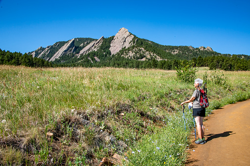 A senior female hiking in Chautauqua Park below the Flatirons has stopped to enjoy the view. The rock formations dominate the foothills of the Rocky Mountains above Boulder. Hikers are visible on the trail
Boulder, Colorado, USA
07/12/2022