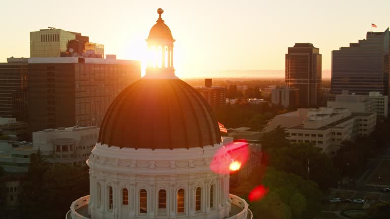 Drone Shot of US and CA Flags Flying Over California State Capitol with Dramatic Lens Flare