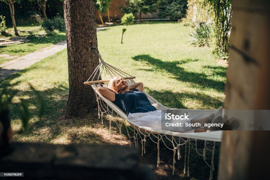 Woman relaxing in hammock One woman, mature female lying in a hammock alone in back yard. Relaxation Stock Photo