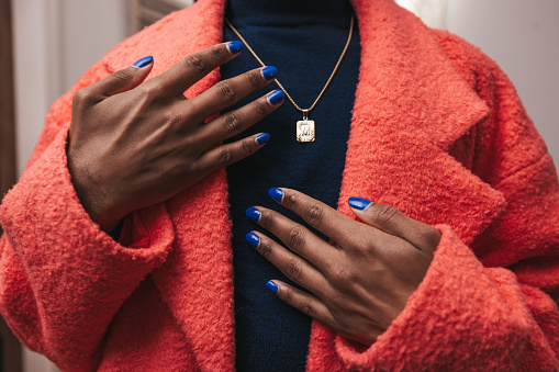 Non-binary person with polished nails getting dressed with a pink jacket. Close up shot on hands.