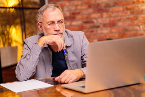 worried aged man sit by laptop and try do make payment online stock photo