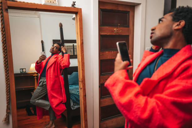 Home portrait of a young Non-Binary person. He/She is wearing a pink colored jacket and dressing looking at the mirror in the bedroom.