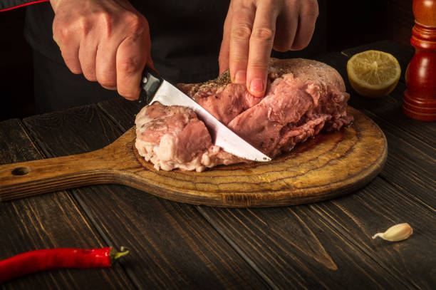 istock Chef cuts meat with a knife before baking. Spices on the kitchen table in a restaurant for preparing a delicious lunch or dinner 1435080330