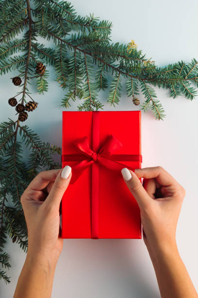 istock Christmas tree branch with red gift box and woman's hand on white background. Minimal creative flat lay. New Year Christmas background concept. 1435080503