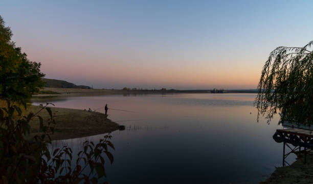 fisherman on the banks of lake budeasa in central romania at sunset - transsylvania imagens e fotografias de stock