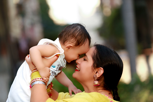 Mother and child of Indian ethnicity playing portrait arm raised outdoor in nature.
