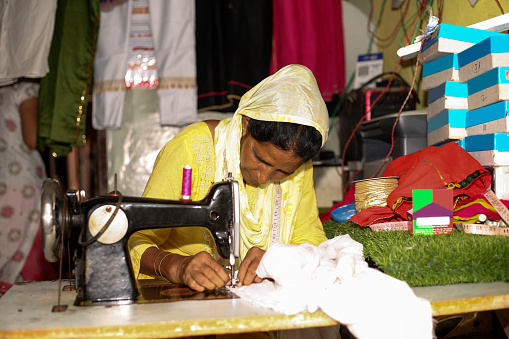 Mid adult Indian tailor stitching clothes at home sitting portrait Indoor close up.