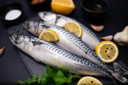 Fresh raw mackerel with lemon and spices on a black stone background
