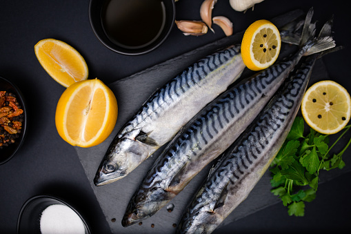 Fresh raw mackerel with lemon and spices on a black stone background