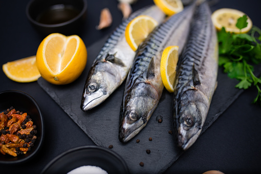 Fresh raw mackerel with lemon and spices on a black stone background