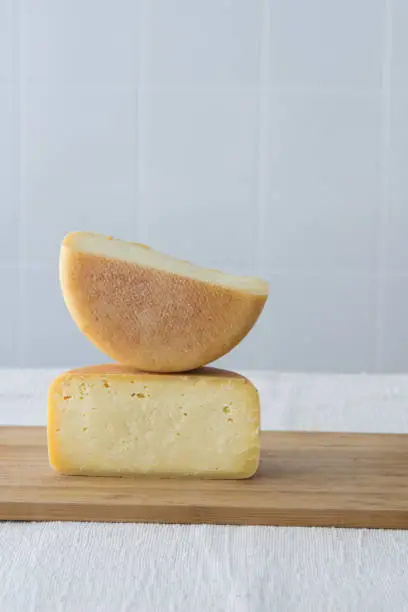 Photo of Cutted round partmesan or pecorino cheese head on wooden board on light background. Fresh dairy product, healthy organic food, selective focus, copyspace. Delicious appetizer.