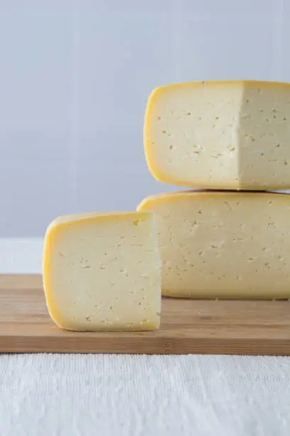 Photo of Cutted round partmesan or pecorino cheese head on wooden board on light background. Fresh dairy product, healthy organic food, selective focus, copyspace. Delicious appetizer.