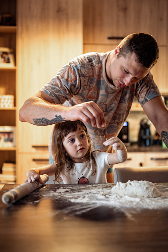 Loving dad showing to his little daughter how to cook tasty bakery cookies or biscuits at home. Father and child daughter knead dough. Baking at home.