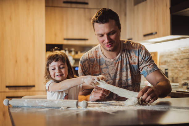 istock Dad with daughters have a fun. Father and child daughter knead dough and bake biscuits. 1435086678