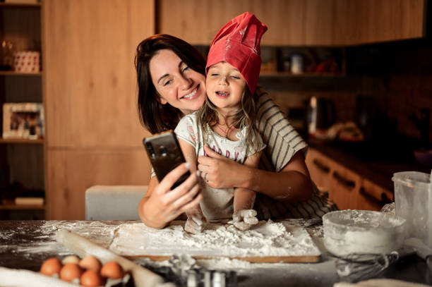 istock Mother and daughter baking in kitchen. Smiling and making selfie.using smartphone while cooking 1435087033