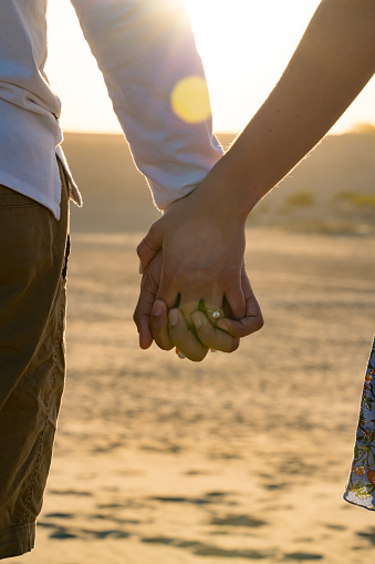 A recently engaged couple holding hands during a stroll through the sand.