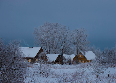Small cozy village with wooden houses in the snow, beautiful winter evening