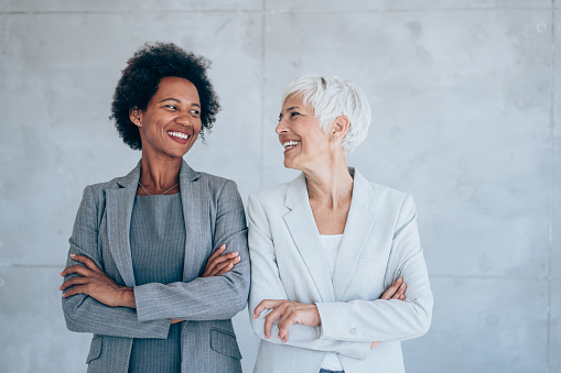 Shot of two confident businesswomen standing side by side and keeping arms crossed while looking to each other.