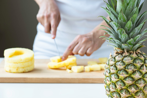 Unrecognizable female is preparing a pineapple snack using a knife and cutting board with a pineapple in foreground.
