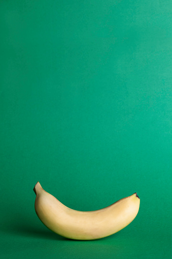 Single yellow banana on green background.