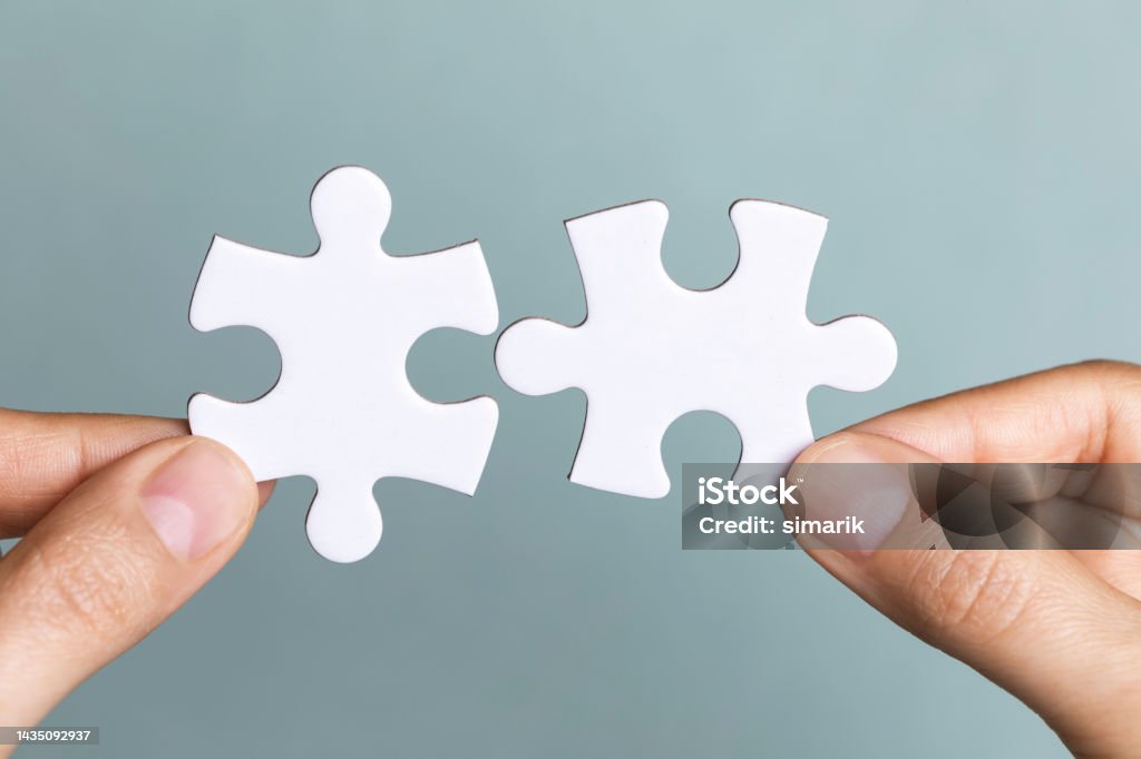Business Teamwork Two hands are holding puzzle pieces in front of blue background. Reconciliation Stock Photo