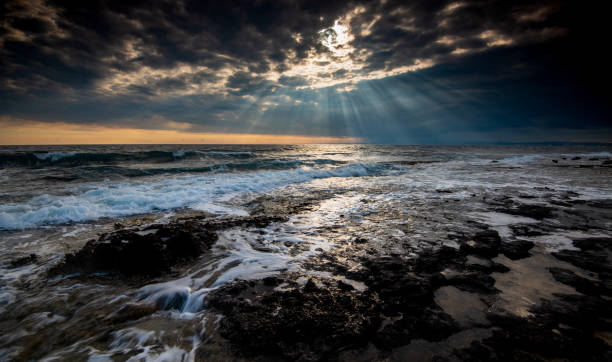 Sunset on a rocky coast. Dramatic cloudy sky wind waves