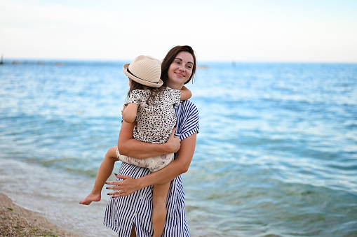 mom with child enjoy summer vacation on the sea. mother with toddler daughter hugging tight on beach. mom hug kid on a seaside beach at sunset during holiday vacation.