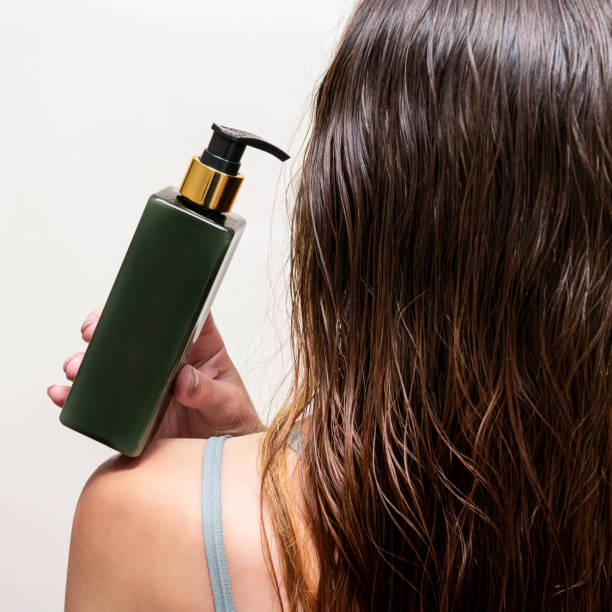 eine frau hält eine flasche shampoo oder haarbalsam auf ihrer schulter neben ihrem nassen haar. - head in hands fotos stock-fotos und bilder