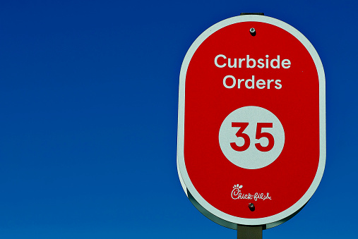 Burke, Virginia, USA - October 20, 2022: Close-up image of a “Curbside Orders” parking sign with number “35” against a clear blue sky at a Chick-Fil-A fast food restaurant.
