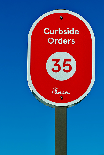 Burke, Virginia, USA - October 20, 2022: Close-up image of a “Curbside Orders” parking sign with number “35” against a clear blue sky at a Chick-Fil-A fast food restaurant.