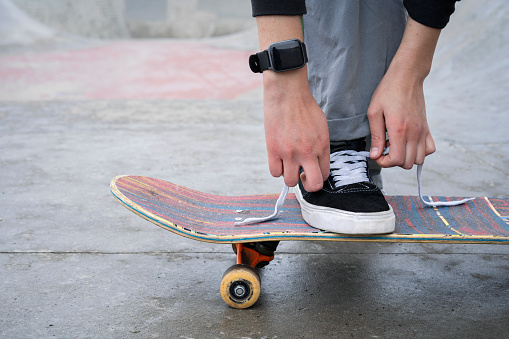Close-up of a young Latina woman's hands tying the laces of her sneakers on a skateboard. Active Latina woman ready to roll on skateboard in a city skatepark.