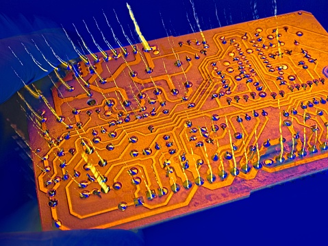 Gold highlighted computer board with electron static charge seeing to bolt upwards from the surface. Computer concept on a blue background.