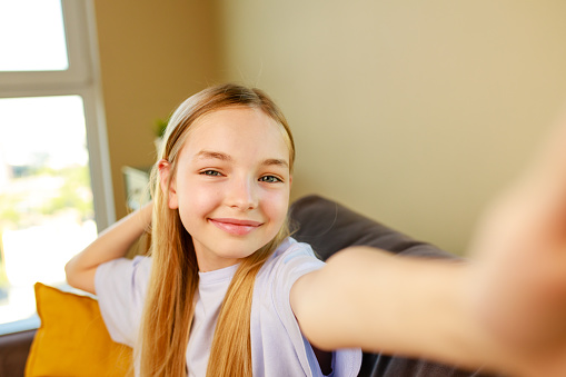 pre-teen girl making selfie photos on her smartphone in cozy living room at home.