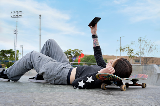 Portrait of a Latin American woman using her mobile phone to take a selfie lying on her skateboard in the skatepark.