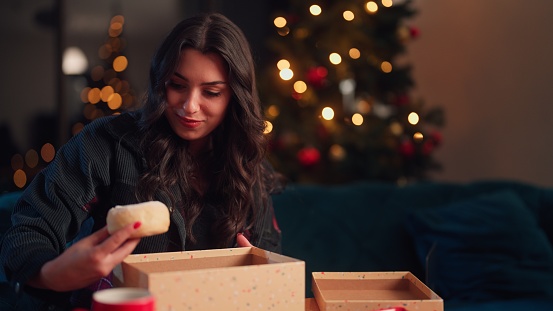 A young woman is opening gift/subscription box in the living room at home during Christmas.