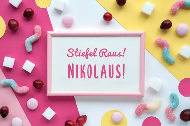 Text Stiefel raus Nikolaus means St. Nicholas day take shoes off. Sweets, chocolates, confectionery on pink and yellow paper. Flat lay, top view. Greeting design for December traditional holiday.