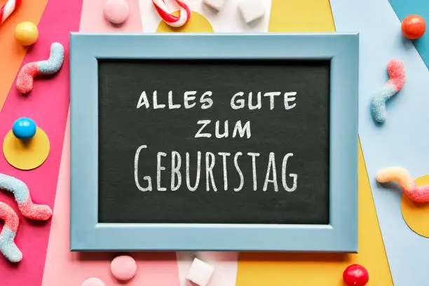 Text Alles Gute zum Geburtstag means Happy Birthday in German language. Text Thank you in frame on layered colored paper. Assorted sweets, candy canes around blackboard. Flat lay chalk board frame.