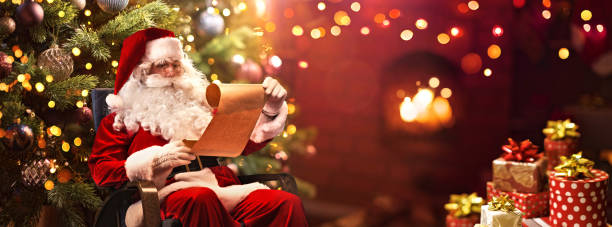 babbo natale seduto nella sua stanza e leggendo la lista dei desideri di natale - babbo natale foto e immagini stock